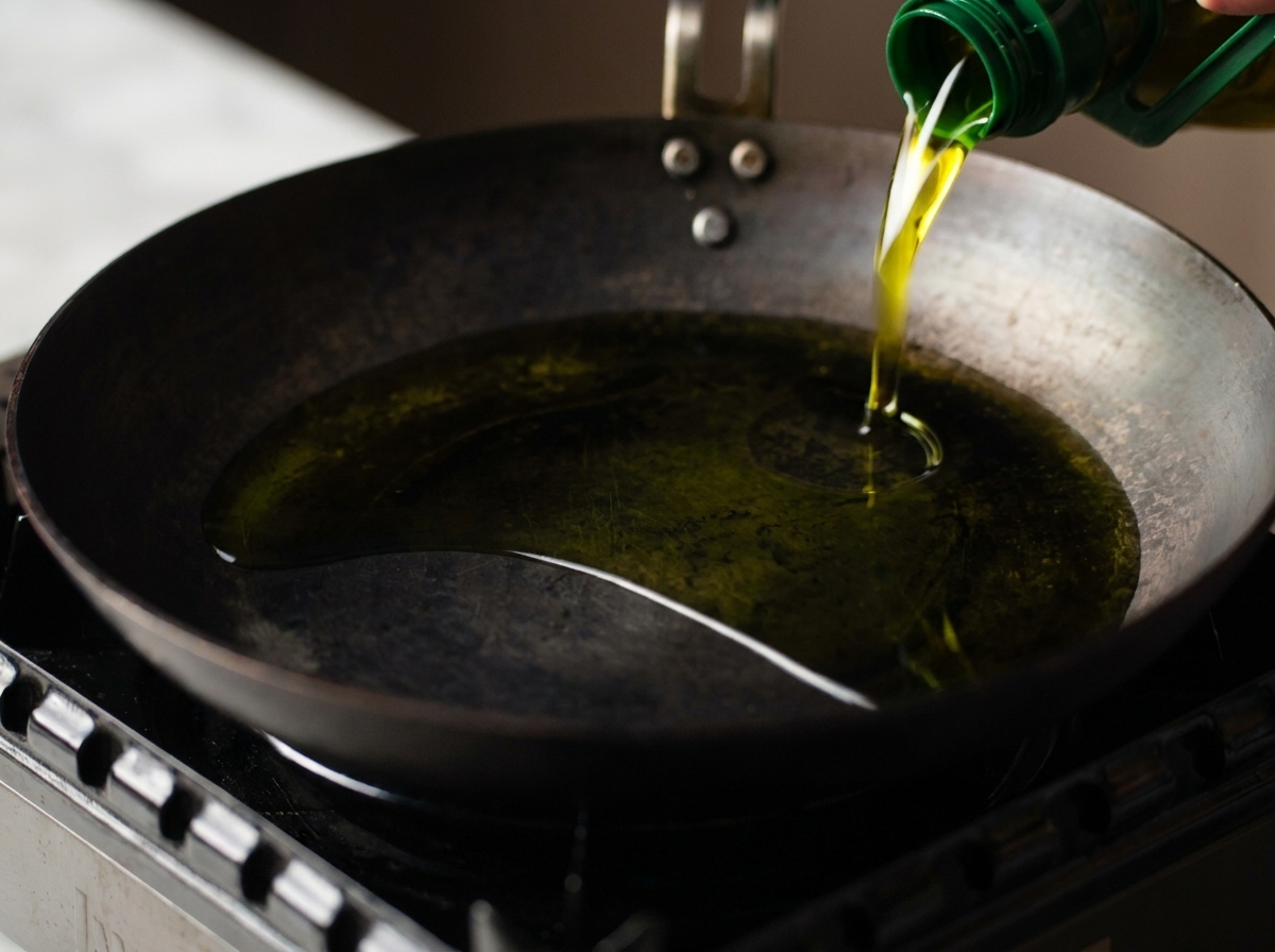 De lhuile de cuisson versée dune bouteille verte dans une poêle en acier carbone bien chaude.
