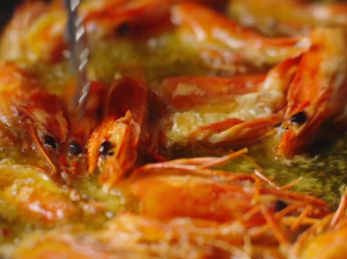 Une pince de cuisine pressant les têtes de crevettes orange vif dans lhuile bouillante.
