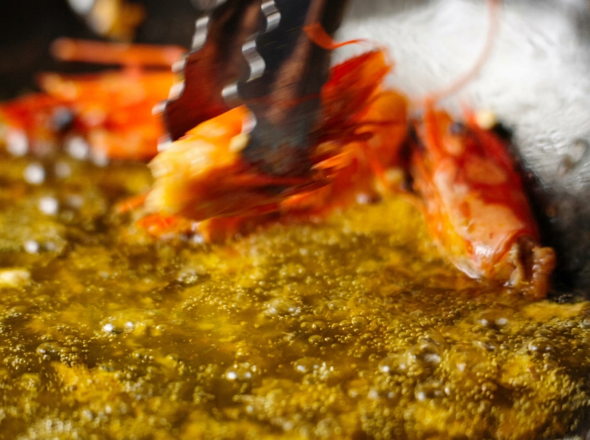 Une pince retirant une tête de crevette frite dune poêle contenant une huile dun orange profond.