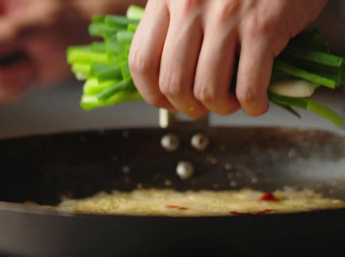 Une main jetant une botte doignons verts hachés dans un wok chaud avec de lhuile frémissante.