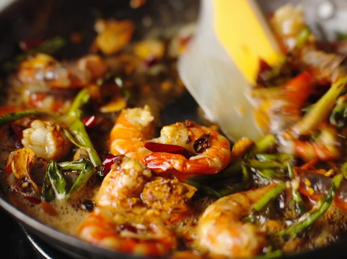 Des crevettes pelées sautées avec de lail, des piments et des oignons verts dans une poêle grésillante.