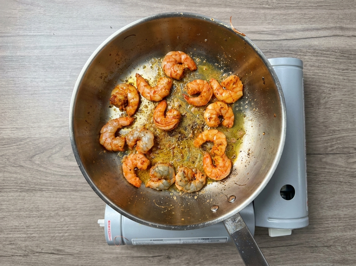 Crevettes épicées cuisant dans une huile infusée rougeâtre.