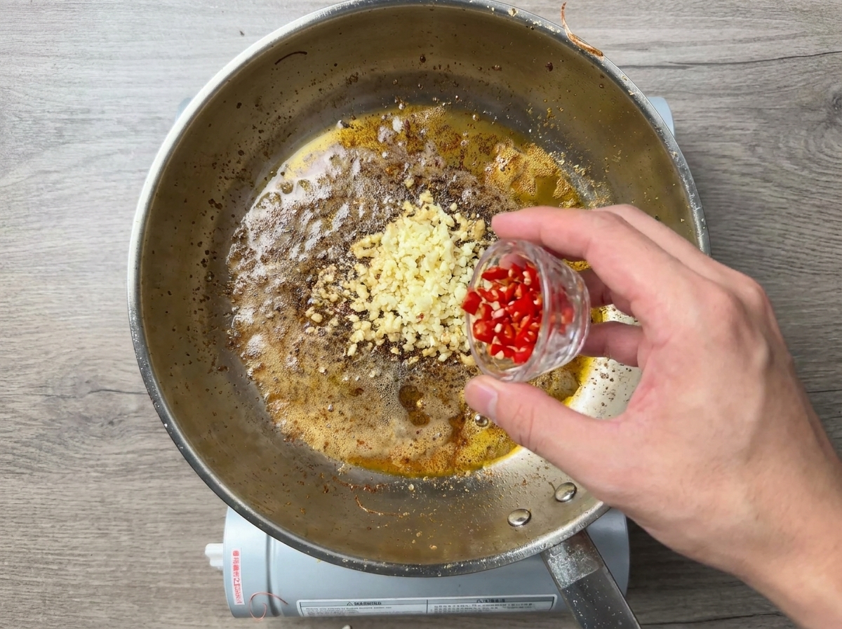 Piment rouge haché ajouté à lail frémissant dans la poêle.
