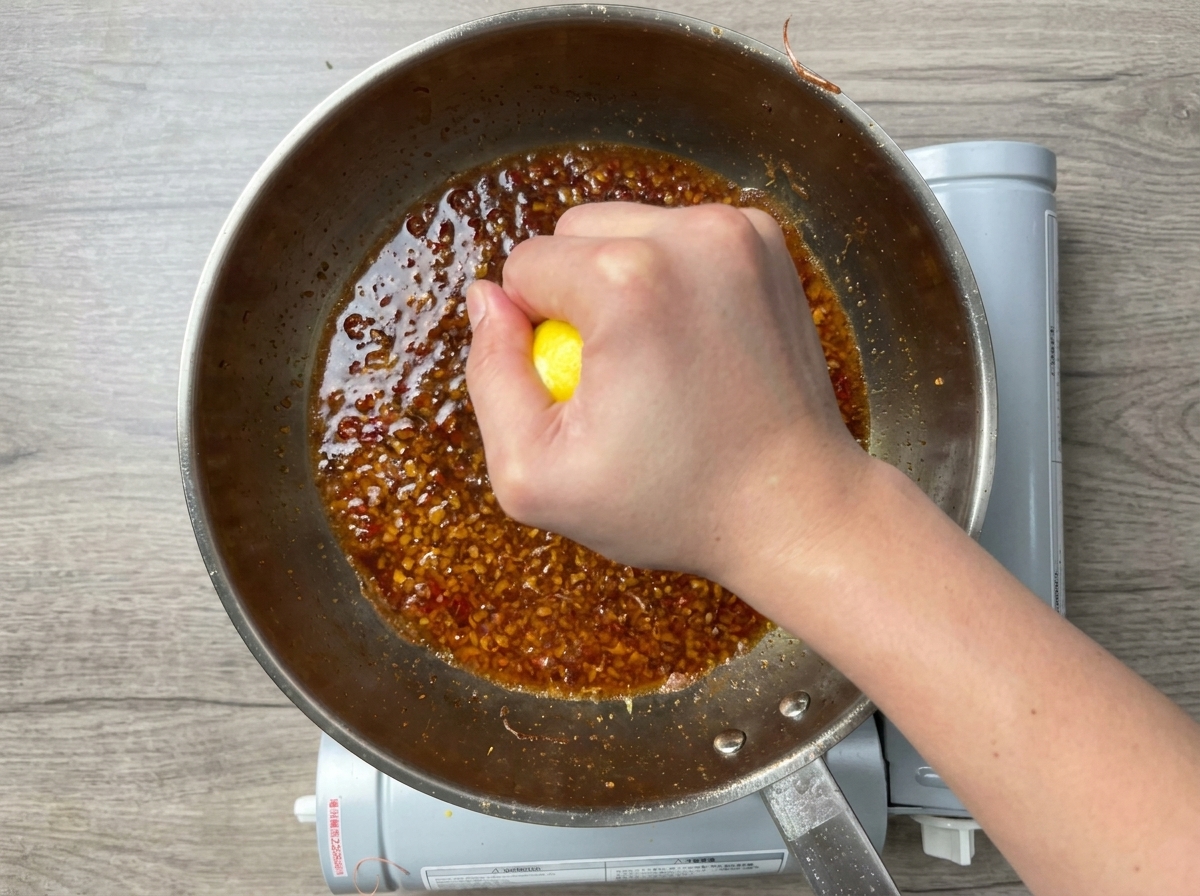 Une main pressant un demi-citron au-dessus dune sauce à lail bouillonnante.