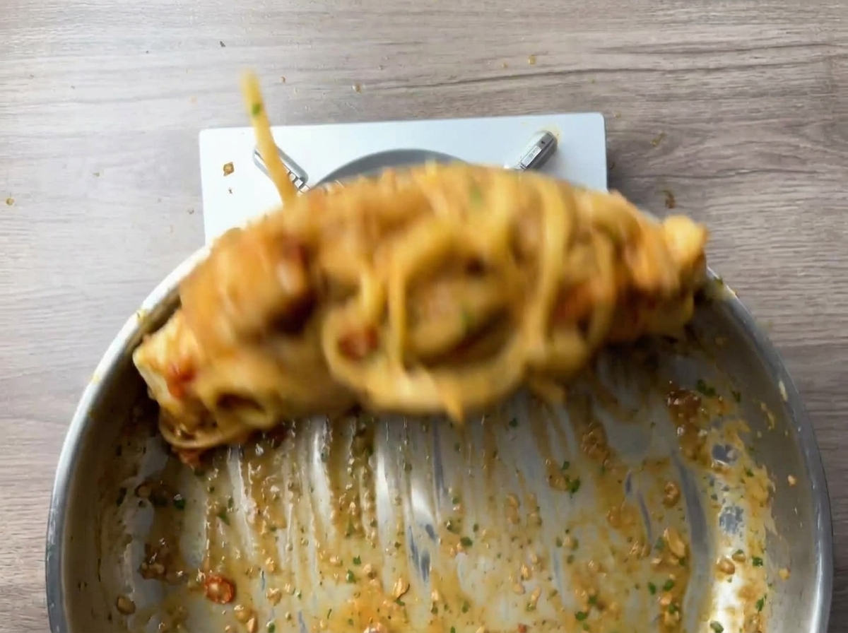 Mouvement dynamique de mélange des pâtes et crevettes dans la poêle.