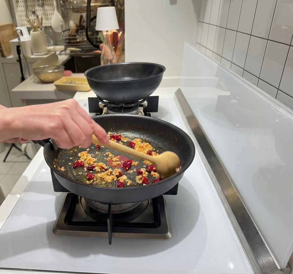 Ail haché et piments séchés ajoutés dans une poêle contenant de lhuile de crevettes rougeoyante.