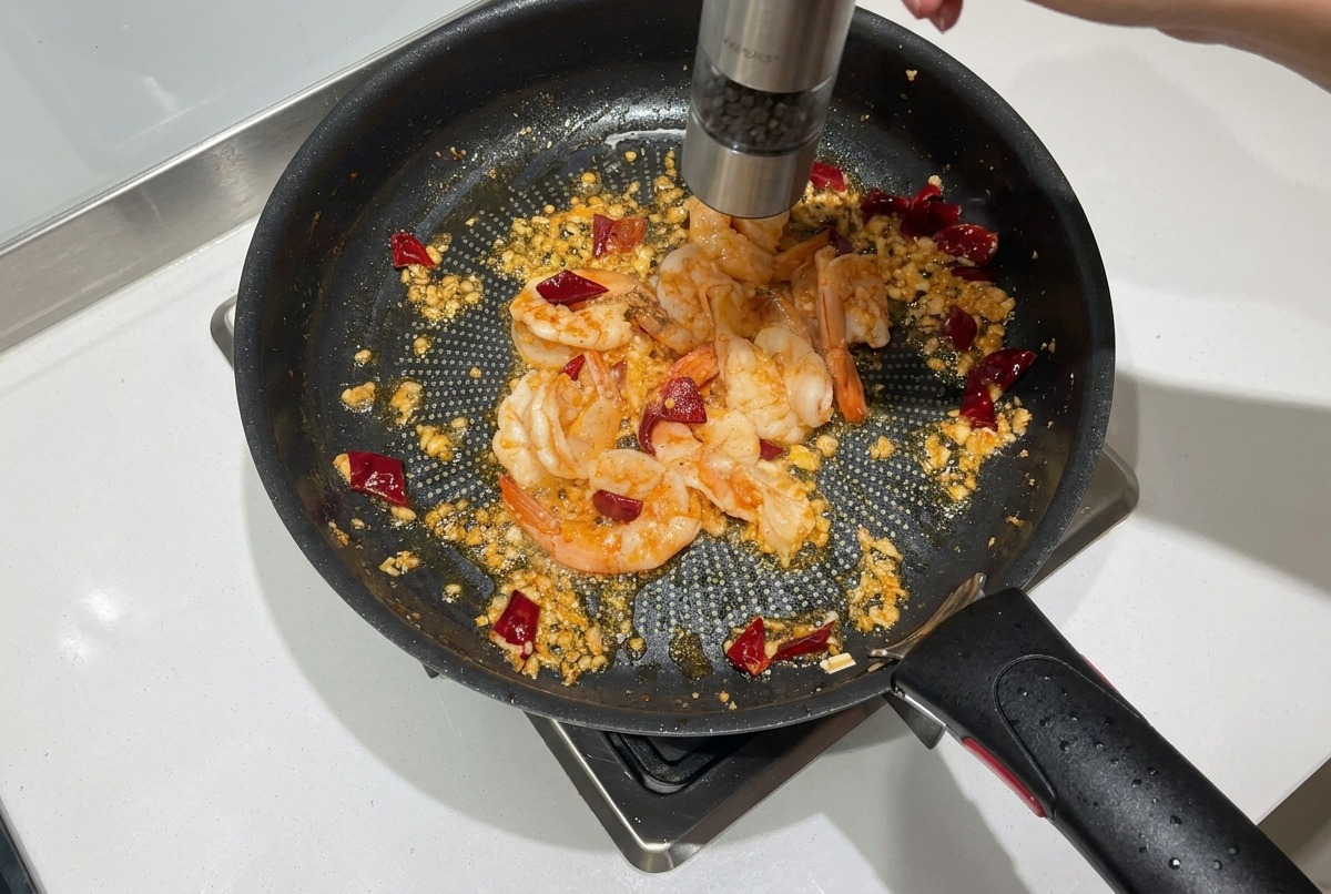 Poivre noir frais moulu au-dessus de crevettes devenant roses dans une poêle.