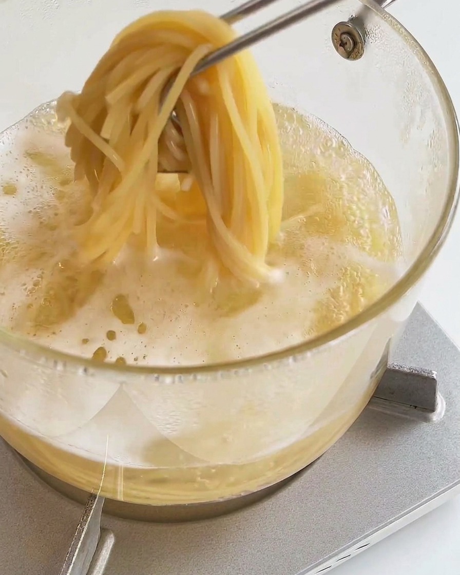 Une pince de cuisine soulevant une portion de spaghetti cuits hors de leau bouillante.
