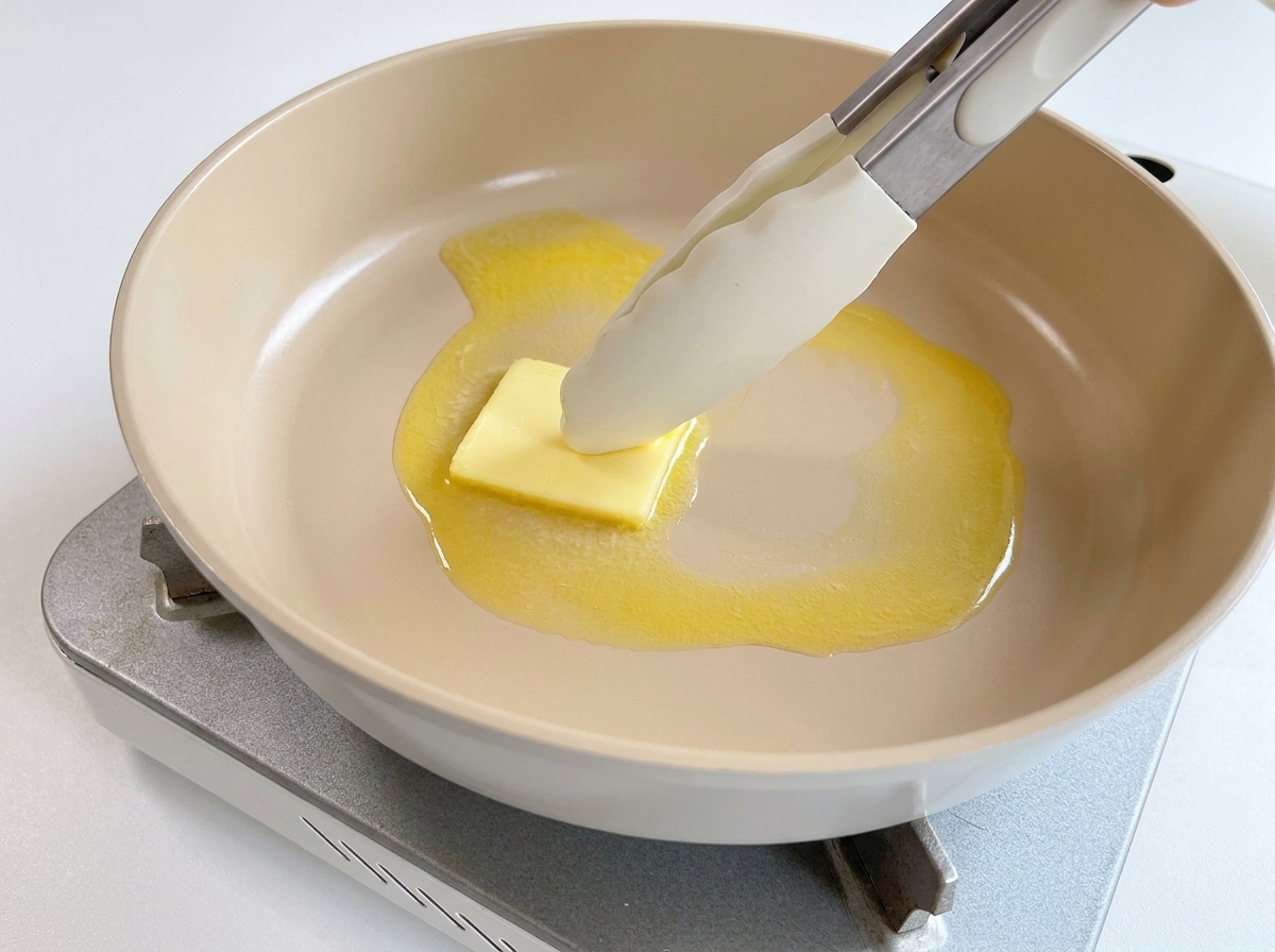 Un morceau de beurre fondant dans une poêle chaude, manipulé avec une pince.