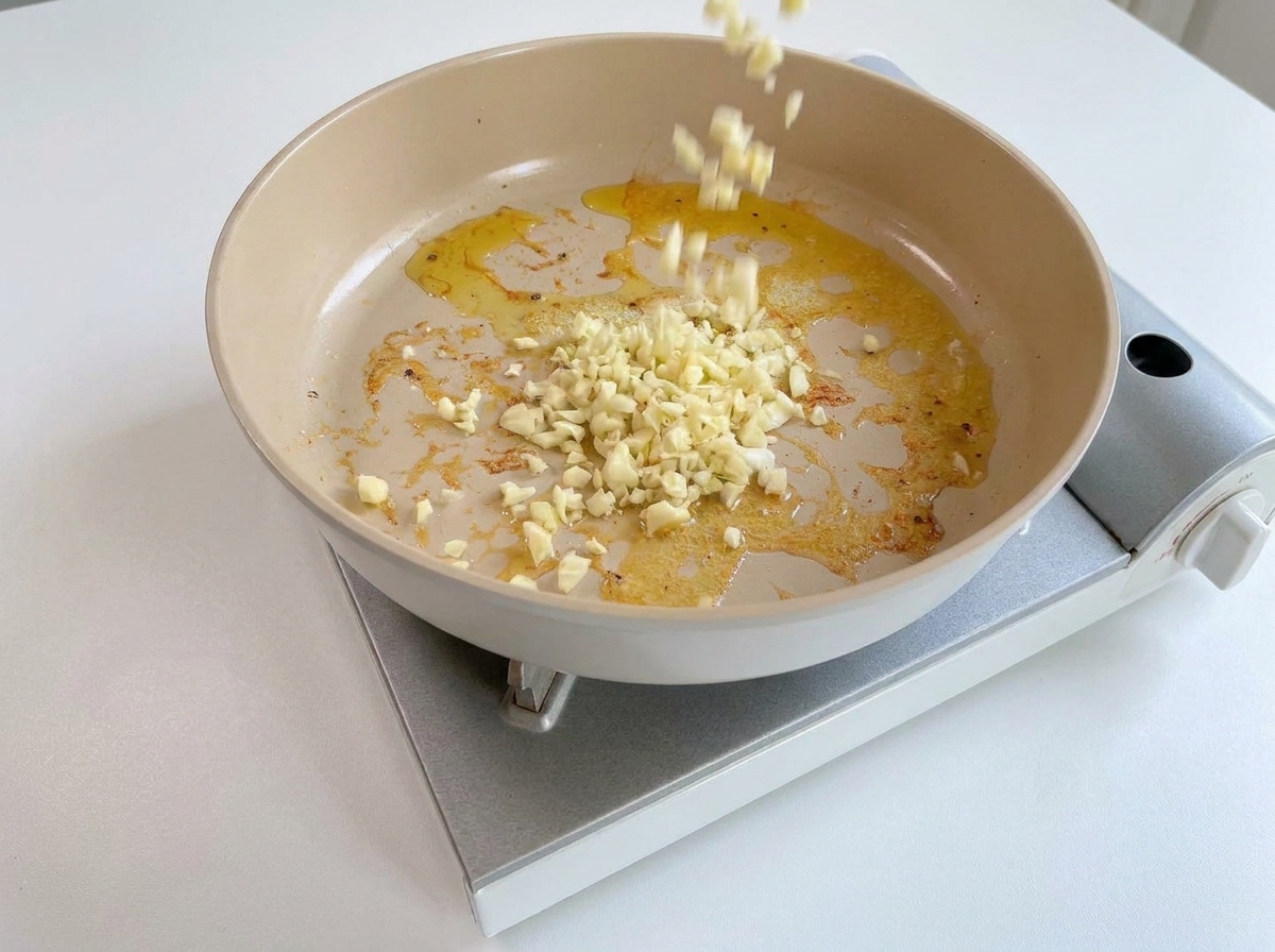 Ail haché versé dans une poêle chaude contenant encore le beurre et le jus des crevettes.
