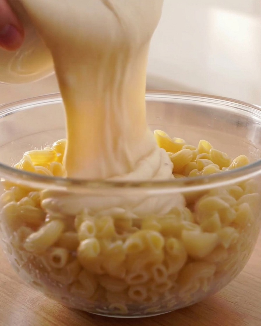 Sauce au fromage onctueuse versée sur des macaronis cuits dans un grand bol.