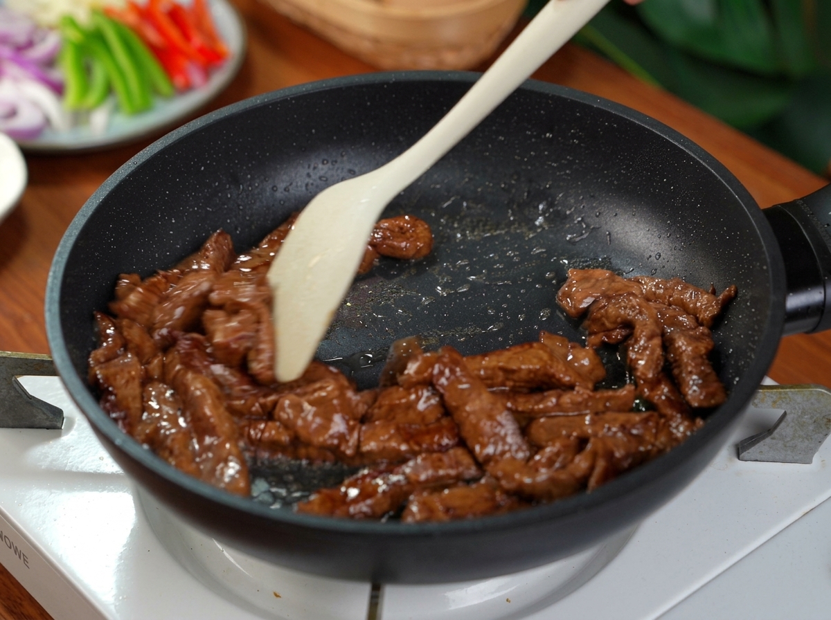 Lamelles de bœuf mariné sautées dans une poêle antiadhésive noire avec une spatule en silicone.