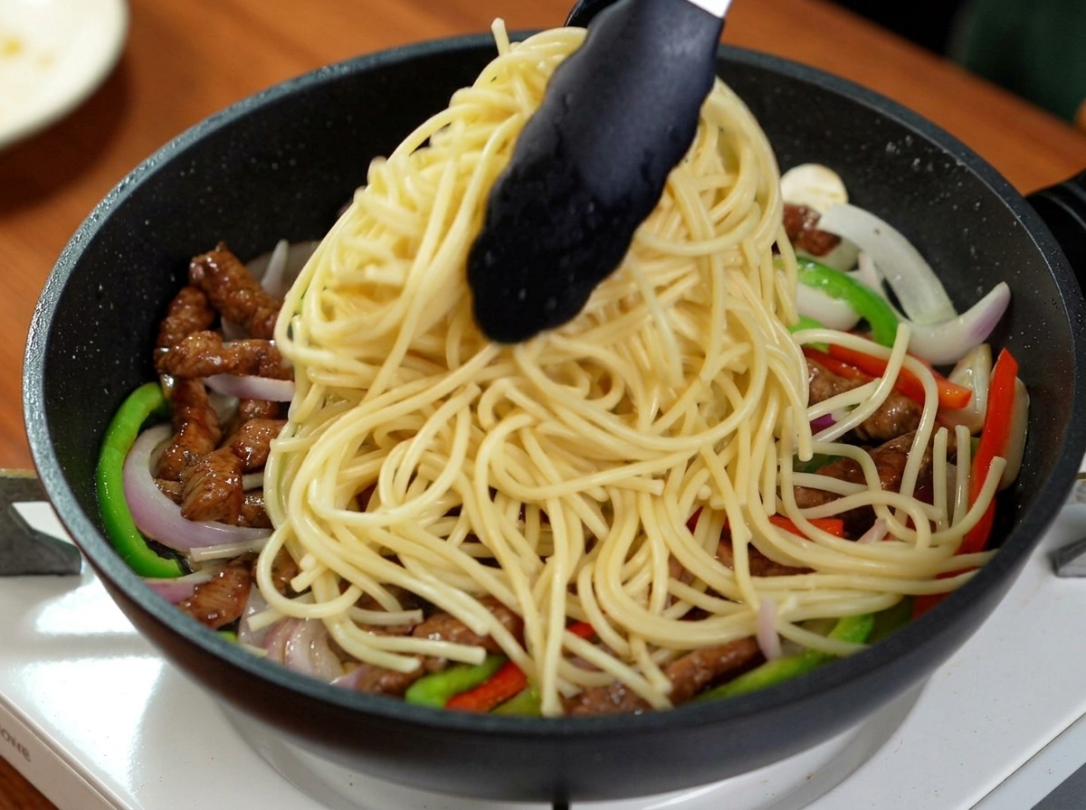 Pinces déposant une portion de spaghetti bouillis sur le mélange de bœuf et de poivrons.