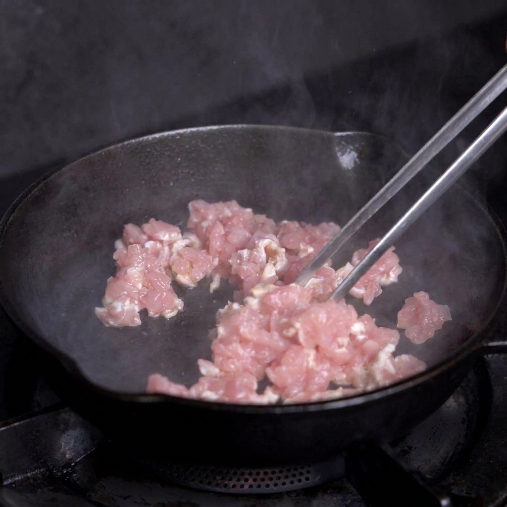 Dés de viande maigre cuisant dans une poêle en fonte chaude, remués avec des pinces métalliques.