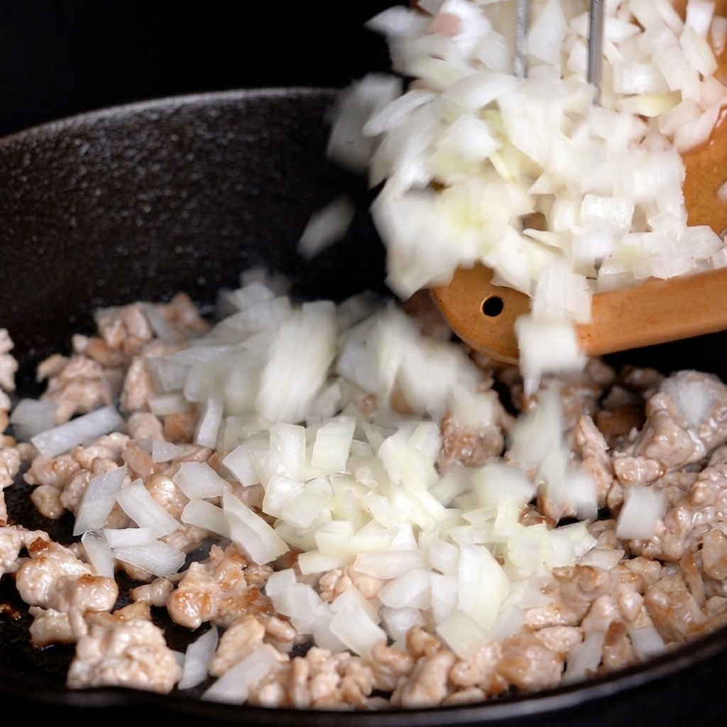 Oignons blancs hachés ajoutés depuis une planche à découper dans une poêle contenant la viande saisie.