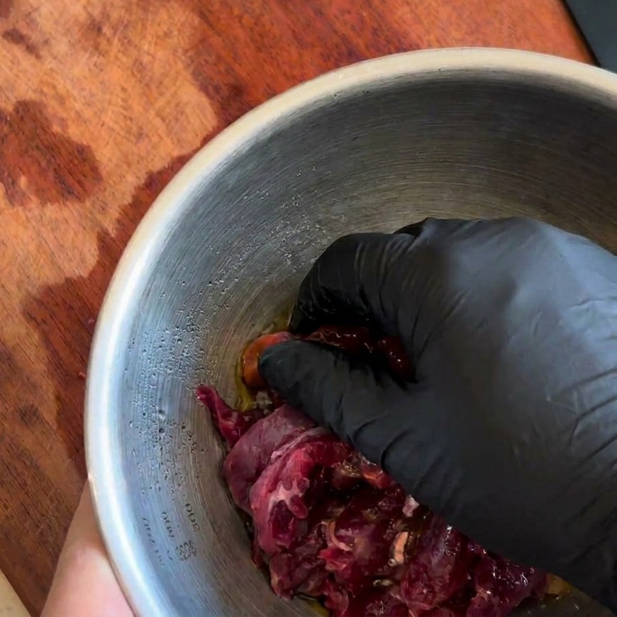 Main gantée mélangeant soigneusement le bœuf avec la marinade foncée.