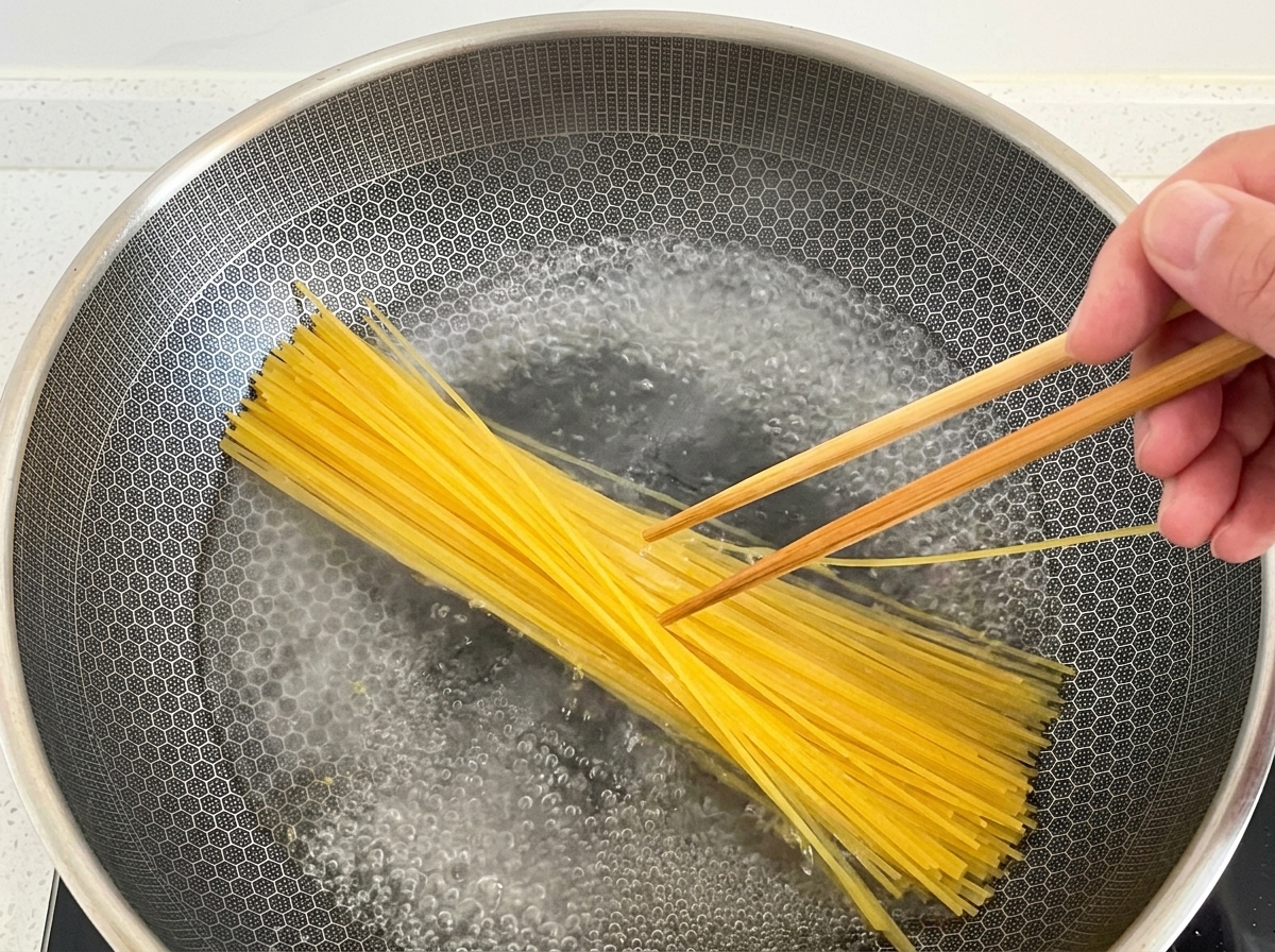 Baguettes en bois immergeant des spaghetti secs dans un wok deau bouillante.