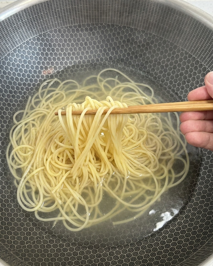 Spaghetti cuits sortis de leau avec des baguettes en bois.