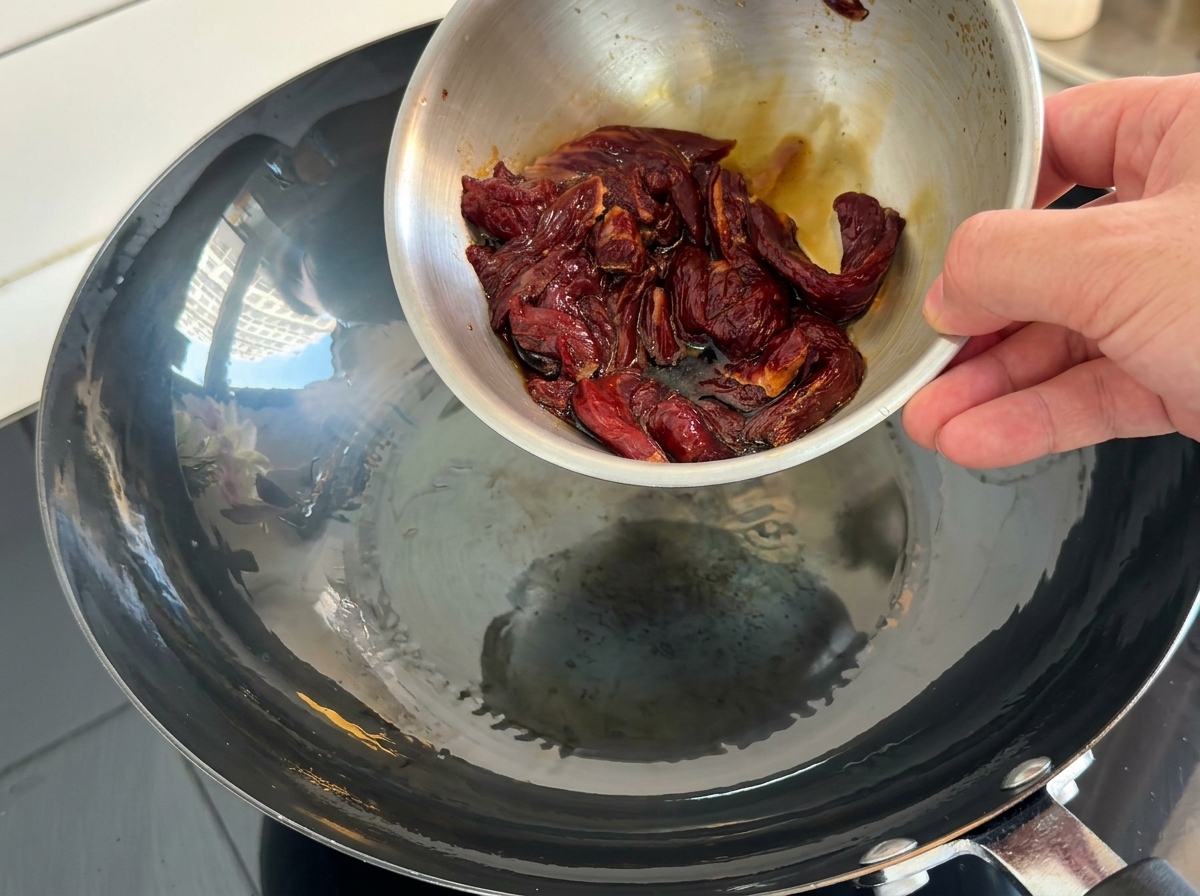 Bœuf mariné versé dans un wok chaud et huilé.