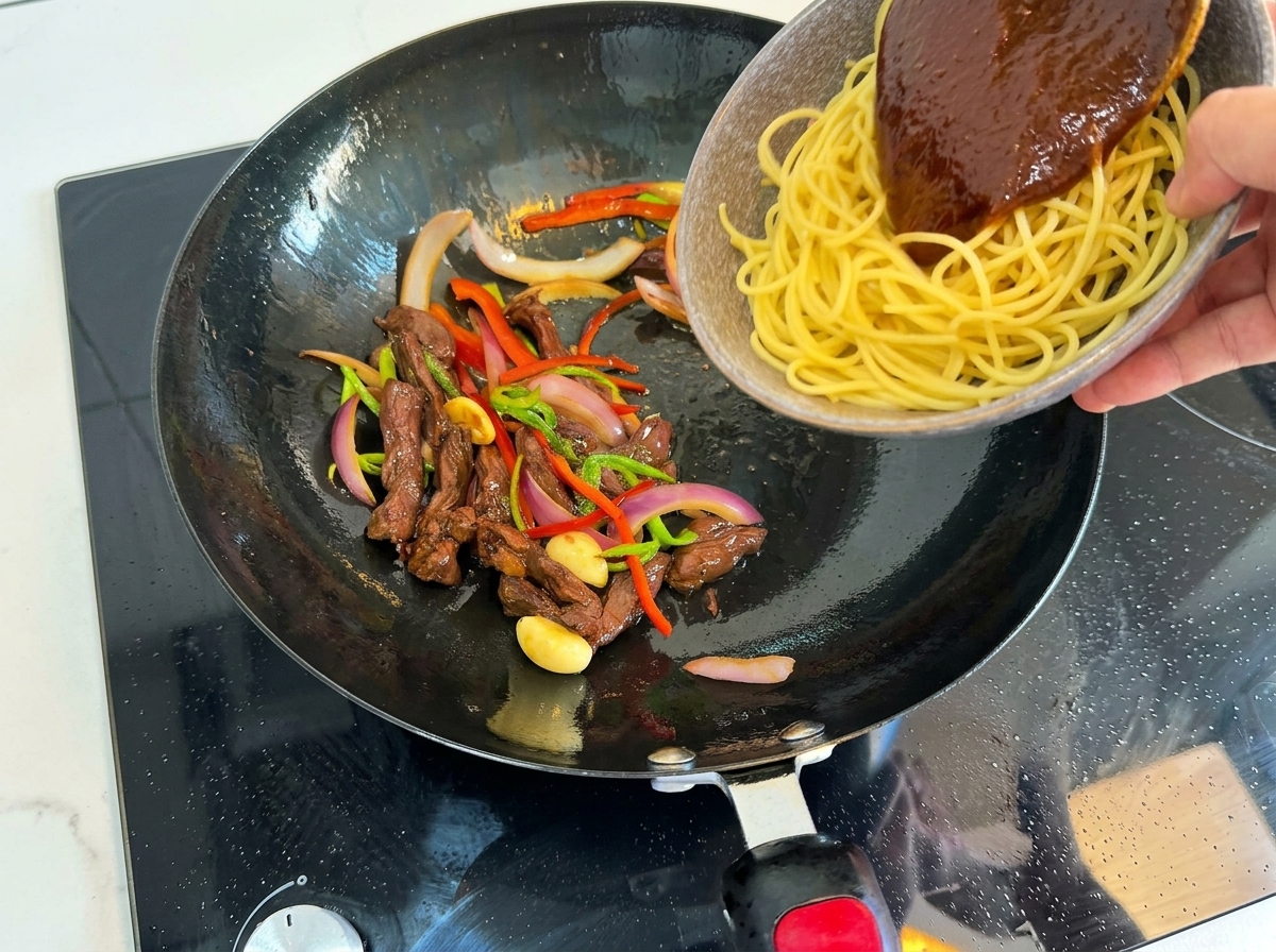 Spaghetti cuits ajoutés dans le wok avec le bœuf et les légumes.