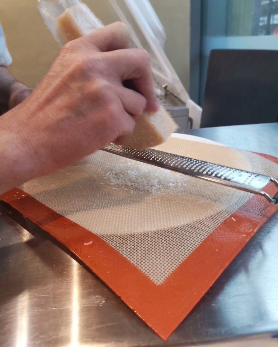 Main râpant un bloc de parmesan sur un tapis en silicone avec une râpe microplane.