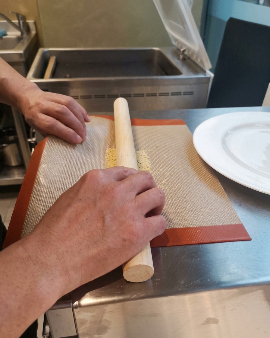 Mains enroulant une tuile de fromage chaude et flexible autour dun rouleau à pâtisserie en bois.