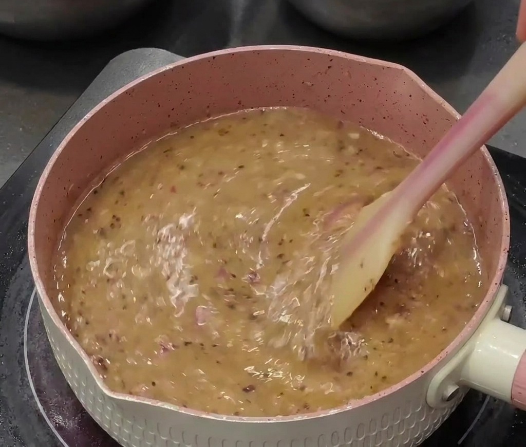 Une sauce au poivre liquide bouillonnant dans une casserole rose, remuée activement avec une spatule.