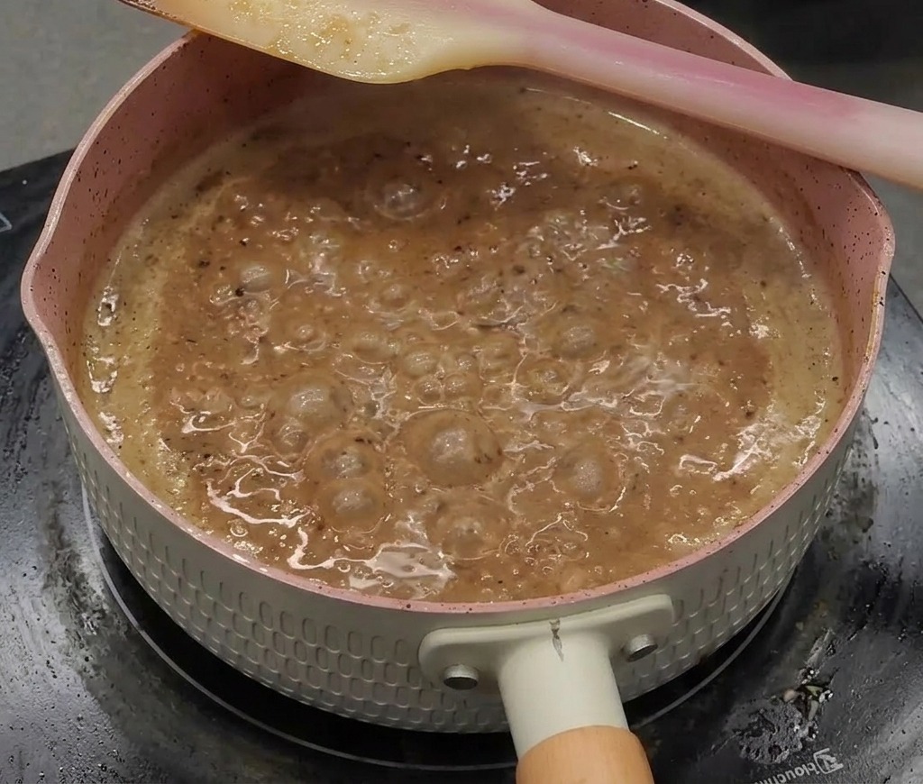 Une sauce au poivre noir épaisse, brillante et sombre bouillonnant vigoureusement dans une casserole.