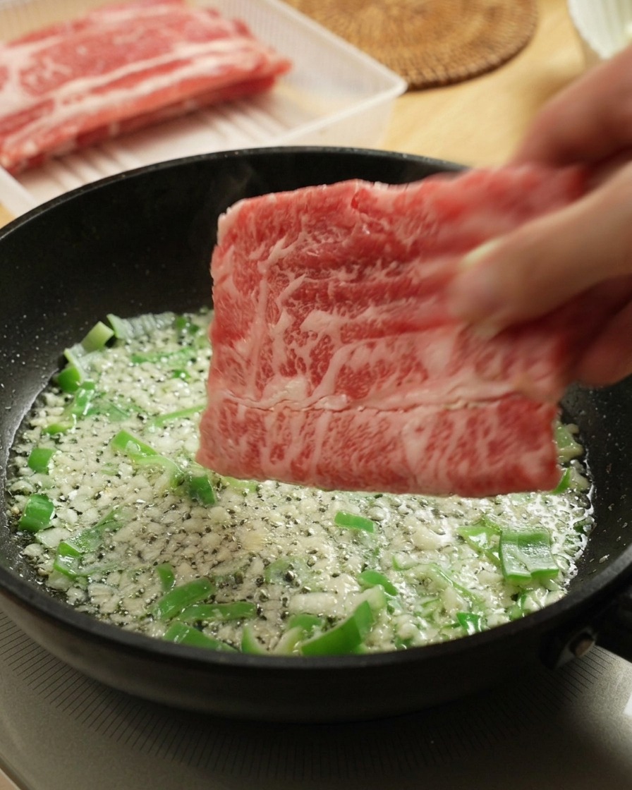 Ajout de fines tranches de bœuf cru dans la poêle avec les aromates.