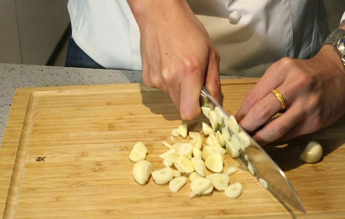 Mains dun chef utilisant un couteau pour hacher grossièrement des gousses dail sur une planche en bois.