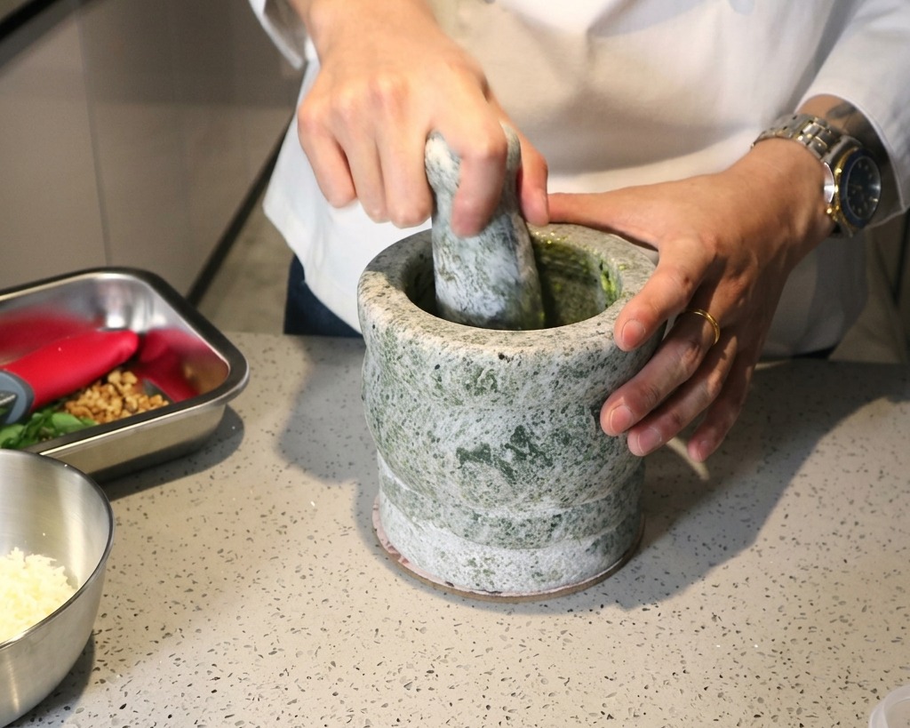 Une personne utilisant un pilon pour broyer des ingrédients frais en une pâte de pesto verte.