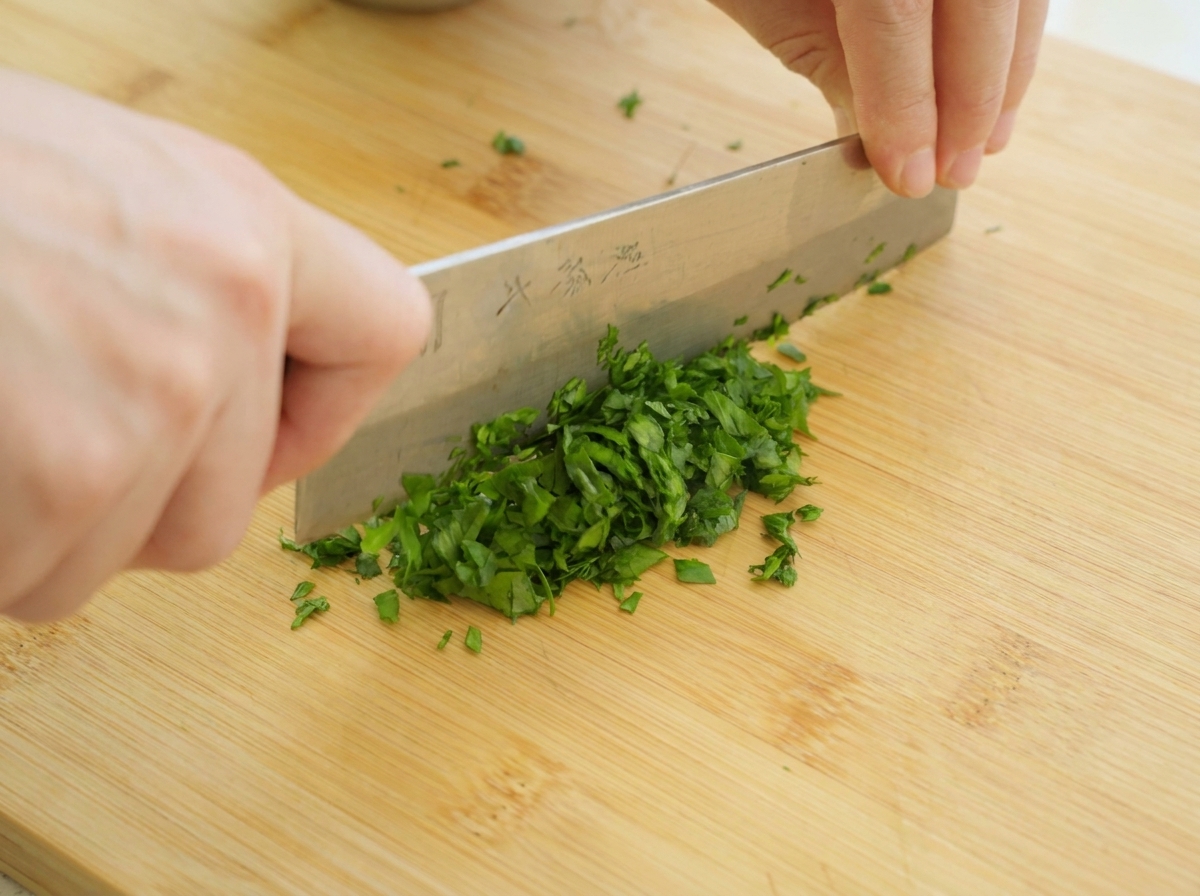 Mains tenant un grand couteau de cuisine, hachant finement des feuilles de persil vert frais sur une planche à découper.