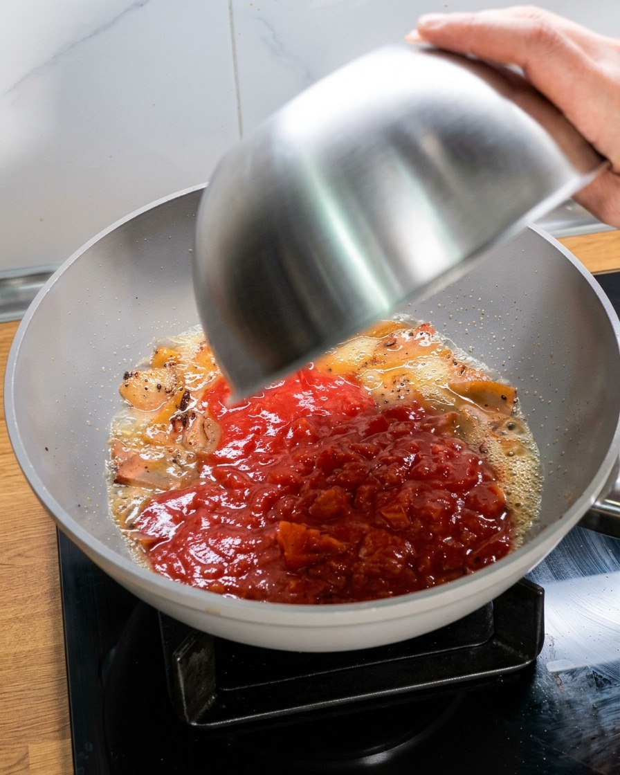 Versement dun bol de tomates écrasées dans la poêle avec la viande et son huile de cuisson.
