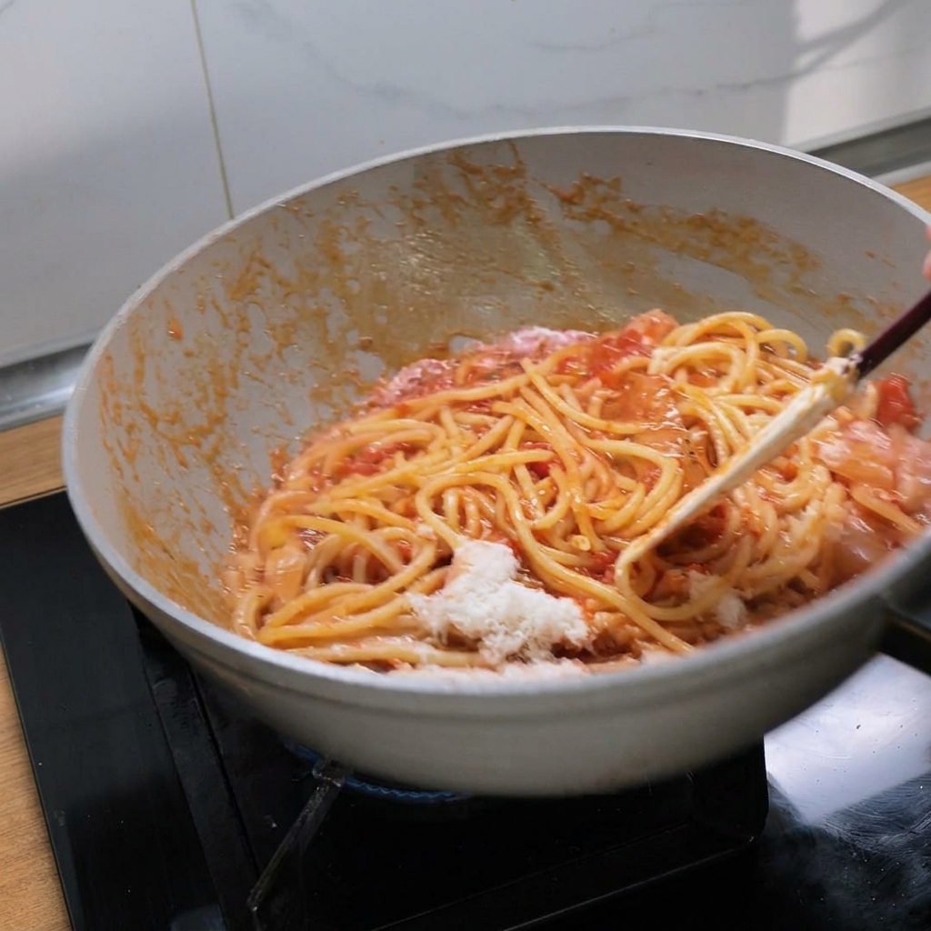 Mélange vigoureux de bucatini avec la sauce tomate riche et le fromage fondant dans une poêle blanche.