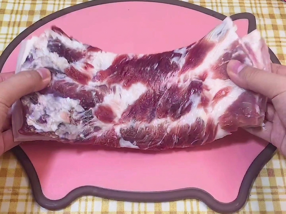 Mains tenant une poitrine de porc crue sur une planche à découper rose en forme de cochon.
