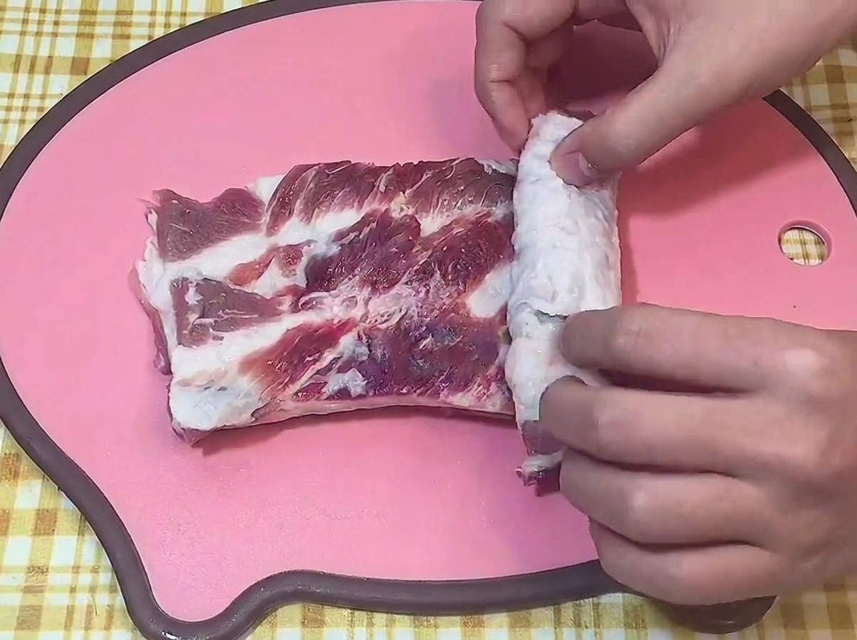 Mains roulant fermement un morceau de poitrine de porc crue sur une planche à découper.