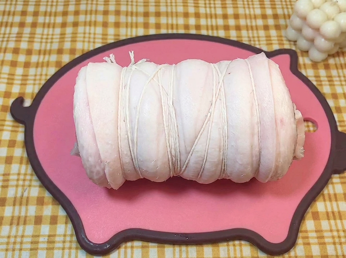 Un cylindre de poitrine de porc crue fermement attaché avec de la ficelle de boucher blanche.