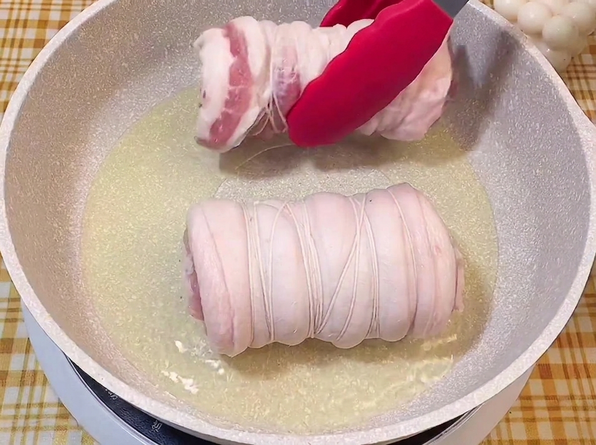 Pince rouge déposant un rouleau de porc ficelé dans une poêle dhuile bouillante.