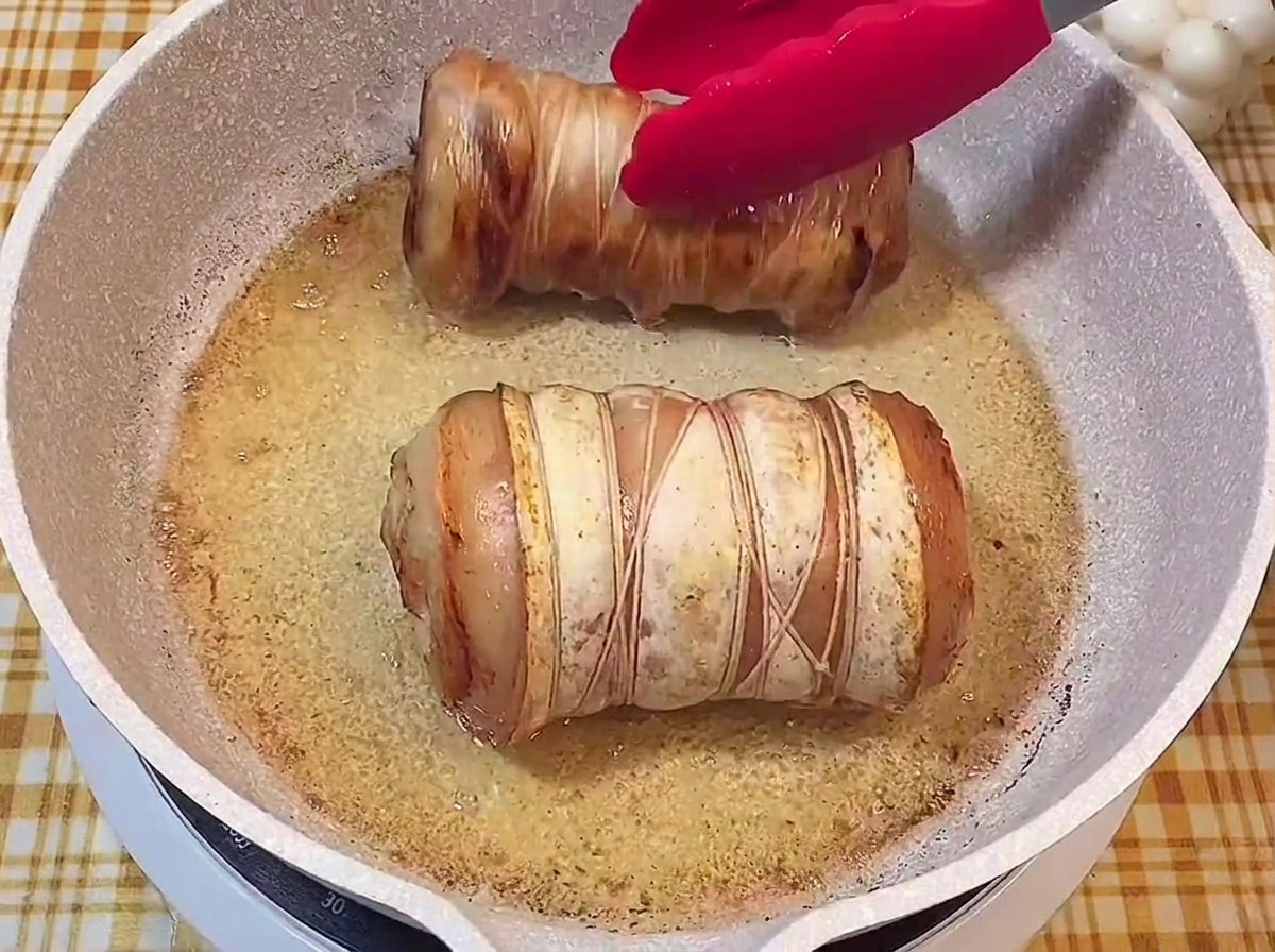 Deux rouleaux de porc ficelés avec une croûte bien dorée et croustillante crépitant dans la poêle.