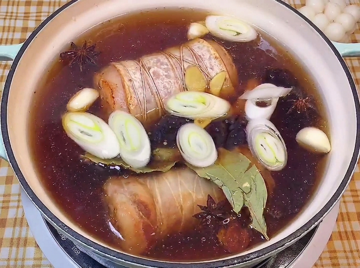 Poitrine de porc roulée et ficelée mijotant dans un bouillon sombre avec des poireaux et des épices.