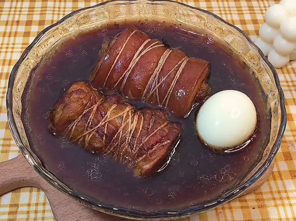 Deux rouleaux de porc braisés et un œuf mollet entier reposant dans un bol en verre de jus de braisage.