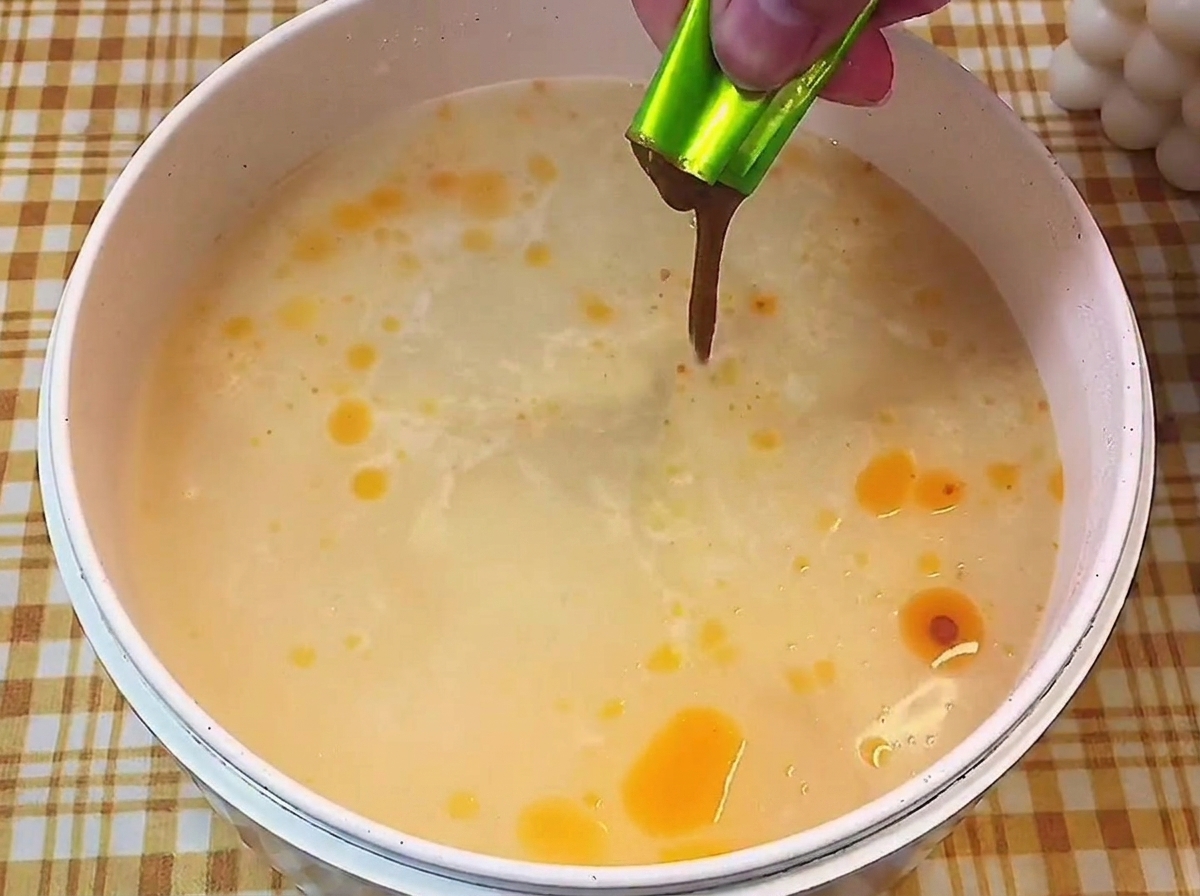 Main versant un sachet dassaisonnement liquide concentré dans une casserole de bouillon clair frémissant.