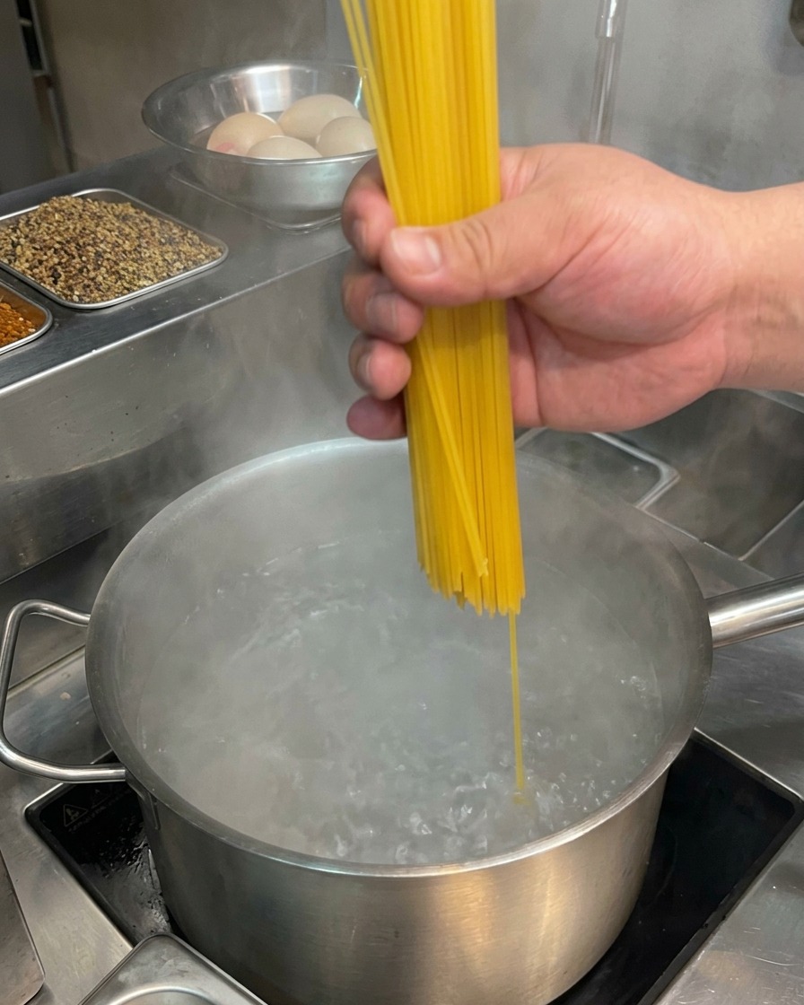Une main plongeant des spaghettis secs dans une grande marmite deau bouillante à gros bouillons.
