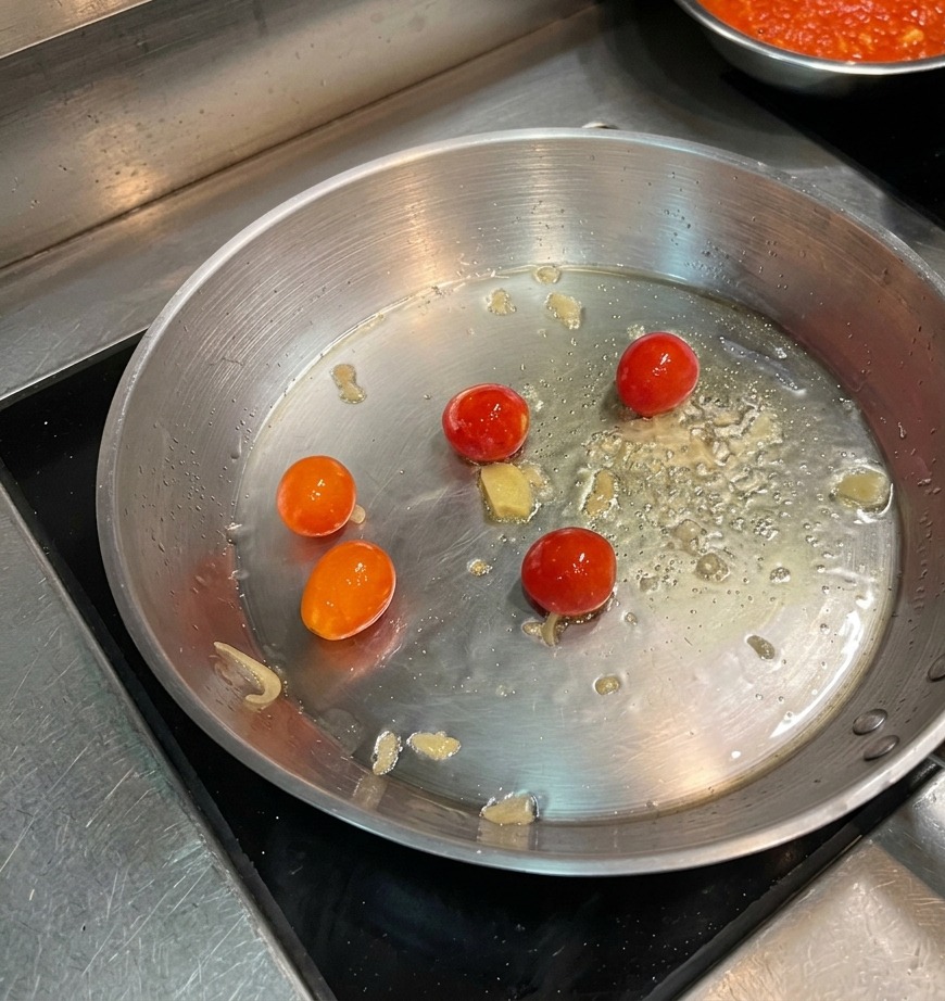Des tomates cerises entières qui se rident dans lhuile chaude dune grande poêle en acier inoxydable.
