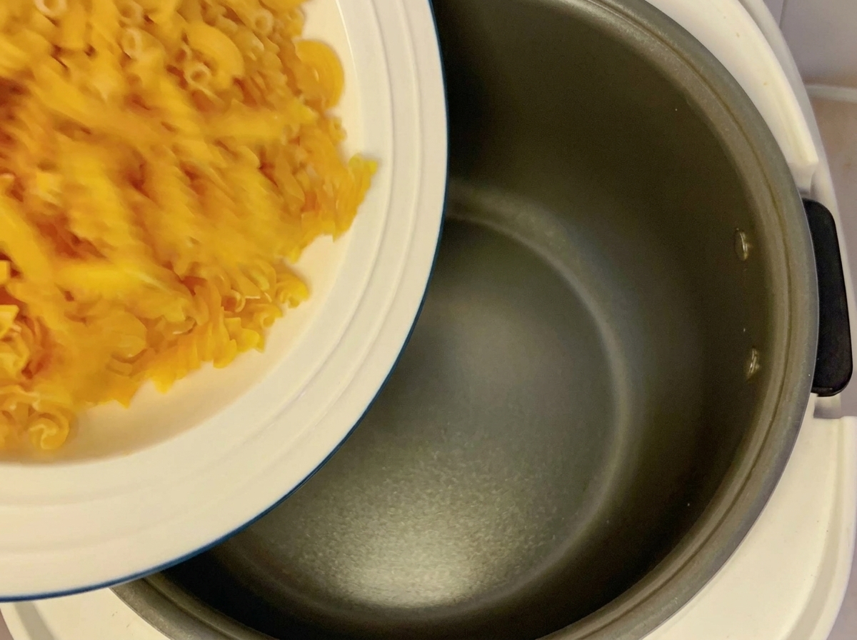 Des pâtes fusilli sèches versées dune assiette blanche dans la cuve vide dun cuiseur à riz.