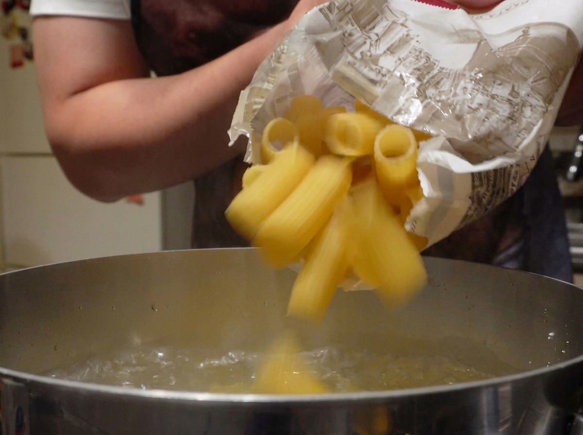 Pâtes rigatoni sèches versées dans une casserole deau bouillante.