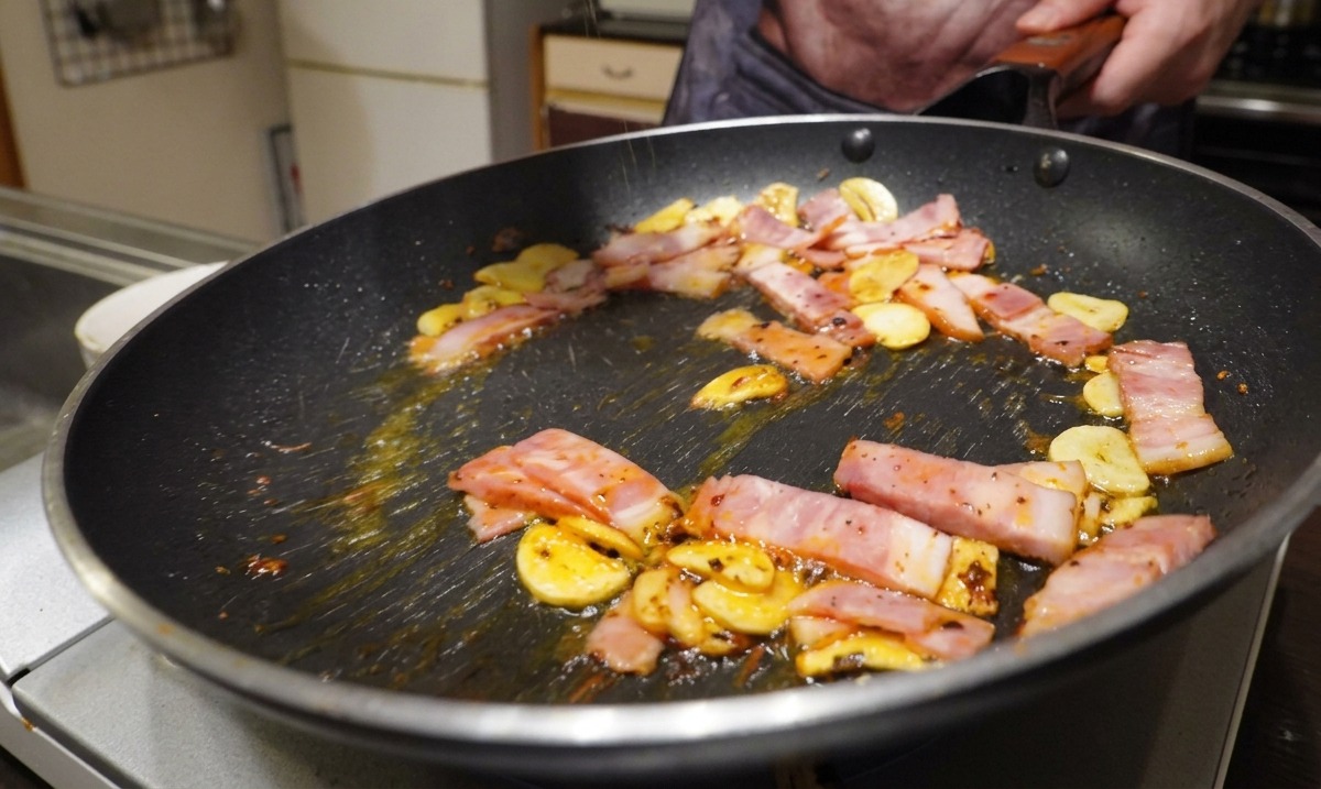Tranches de bacon, ail et piment cuisant dans une poêle tout en étant assaisonnés de poivre noir moulu.