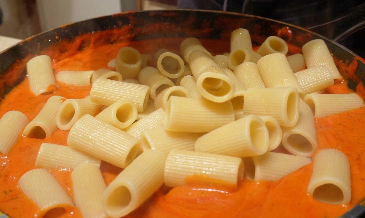 Ajout de rigatoni cuits dans une poêle remplie dune sauce lisse orange-rouge crémeuse.