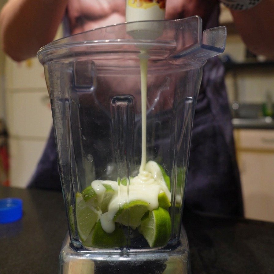 Lait concentré sucré versé sur des citrons verts coupés dans un mixeur.