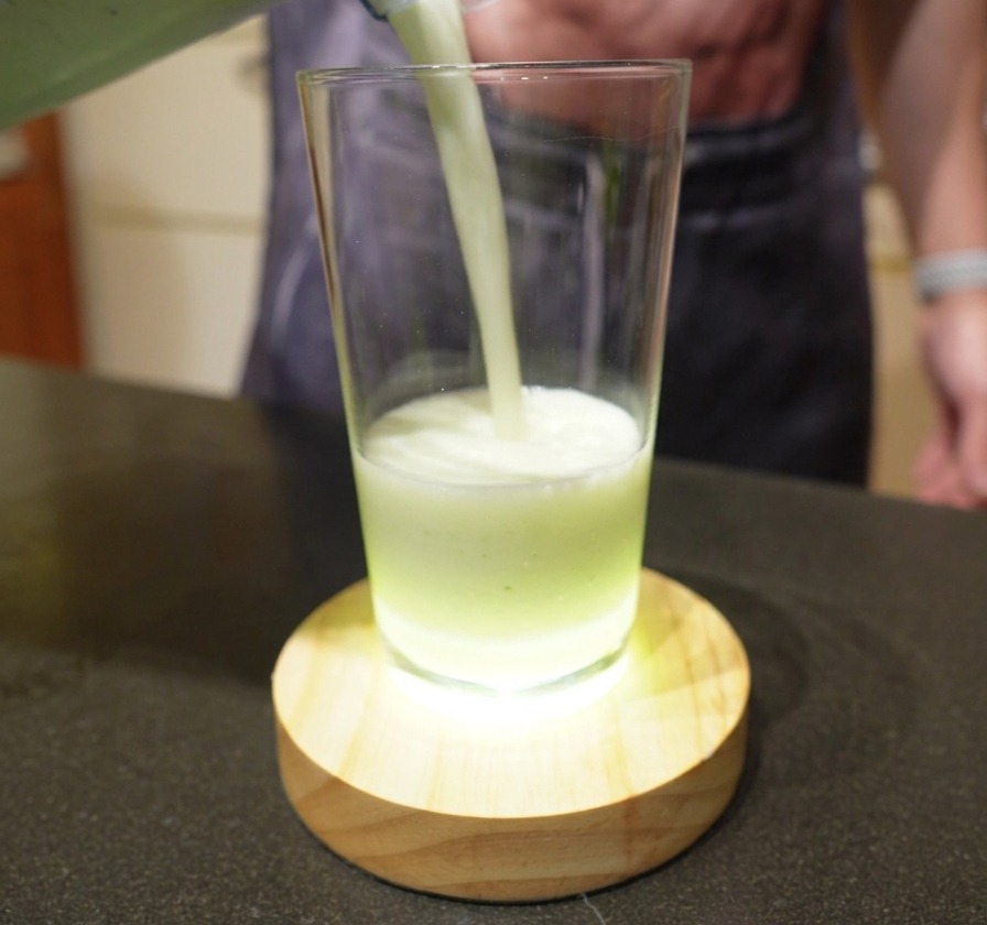 Versement dune boisson crémeuse vert pâle depuis un mixeur dans un grand verre.